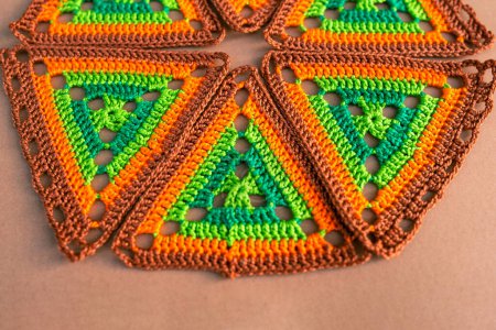 Photo for Close view of crochet triangles in green and orange tones arranged in a circle on beige background. Concept of bright crochet motifs. - Royalty Free Image