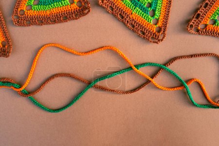 Photo for Top view of tree crochet cords and parts of multicolored crochet motifs on beige background. Textile pieces in orange, green and brown colors. - Royalty Free Image