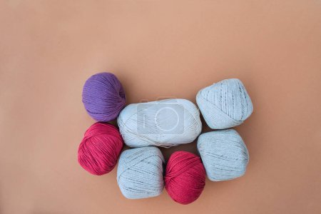 Foto de Vista superior de madejas de hilo beige, blanco, rojo brillante y violeta, colocadas sobre un fondo beige cálido. Los hilos son de diferentes texturas y materiales. - Imagen libre de derechos