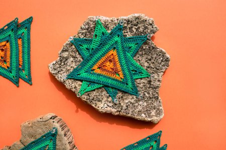 Photo for Three crochet triangle motifs placed on one another to set shape on piece of palm bark with an orange surface underneath. Blocking crochet motifs with pins. - Royalty Free Image