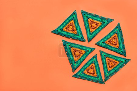 Photo for Top view of multicolored crochet patterns placed on orange background with free place on the left. Bright and vivid ornaments. - Royalty Free Image