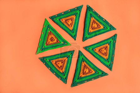 Photo for Crochet triangle motifs, arranged in a shape of circle on ogange background. Color scheme is orange-green. - Royalty Free Image