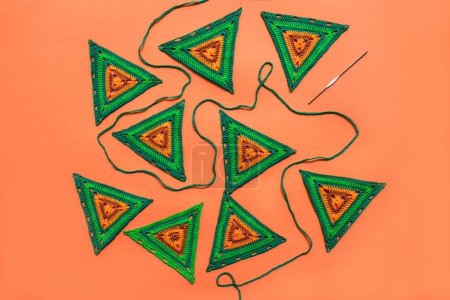 Photo for Top view on green crochet motifs of triangle form,  green crochet cord and a hook on solid orange surface. Crocheting granny triangles. - Royalty Free Image