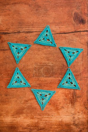 Photo for Blue triangle crochet motifs laid in a shape of a circle on grunge wooden surface. Concept of playing with crothet patterns. - Royalty Free Image