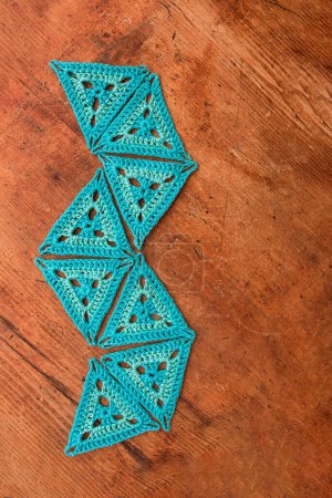 Photo for Top view of blue triangle crochet patterns laid in a random geometric shape on wooden surface. Idea of playing with crothet patterns. - Royalty Free Image