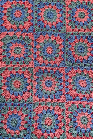 Téléchargez les photos : Vue du dessus des carrés granny crochet afghan en rouge, bleu et vert décoloré couleurs. Texture motif au crochet avec une couleur rouge fanée comme principale. - en image libre de droit