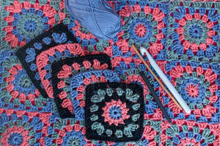 Téléchargez les photos : Vue du dessus des carrés de mamie avec des bordures noires, crocheter des crochets de différentes tailles et écheveau de fil bleu sur la texture du crochet multicolore afghan. - en image libre de droit