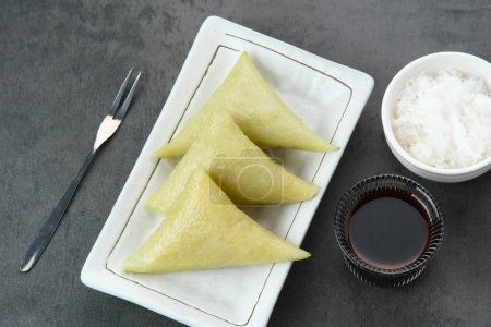 Téléchargez les photos : Lupis ou Lopis, un aliment traditionnel indonésien fabriqué à partir de riz collant et enveloppé dans des feuilles de banane. Servi avec noix de coco râpée et sucre brun liquide. - en image libre de droit
