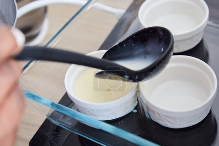 Foto de Negro cuchara verter crema Brulee mezcla en blanco Ramekins - Imagen libre de derechos