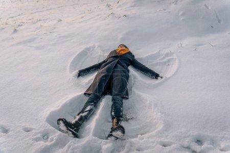 Téléchargez les photos : Une femme couchée dans la neige sous la forme d'un ange de la neige en hiver. - en image libre de droit