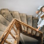 A woman looks up standing on an old wooden staircase.