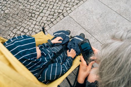 Téléchargez les photos : Vue du dessus d'une femme tapant un message sur son téléphone, près d'une poussette avec un enfant. - en image libre de droit