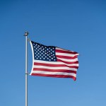 The flag of the United States of America flutters in the wind against a clear blue sky. Waving USA flag.