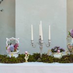 Decorative decoration of the festive table. Candlestick with candles, vases with hyacinths and other flowers, green moss on a table covered with a white tablecloth.