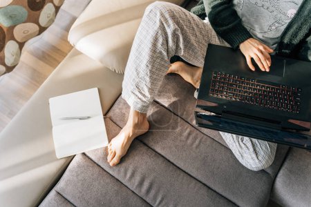 Vue du dessus d'une femme en pyjama avec ordinateur portable et bloc-notes.