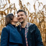 A woman kisses a man on the cheek during a romantic walk in a cornfield.