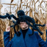 Huge black toy spider on a woman's head in a cornfield during a Halloween party in a cornfield.