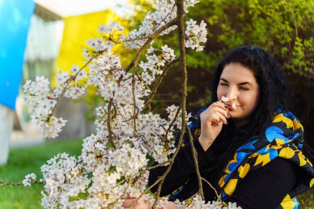Young Ukrainian brunette woman enjoying the aroma of cherry blossoms while walking in the park in spring.
