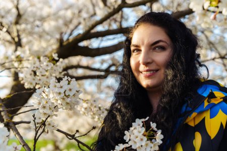 Attractive young brunette woman with long hair smiling in spring in blooming cherry blossom garden.