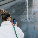 Woman taking pictures of fountain with mobile phone while walking around the city.