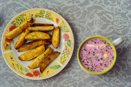 A bowl of popular Lithuanian cold beetroot soup Saltibarsciai with baked potato wedges.