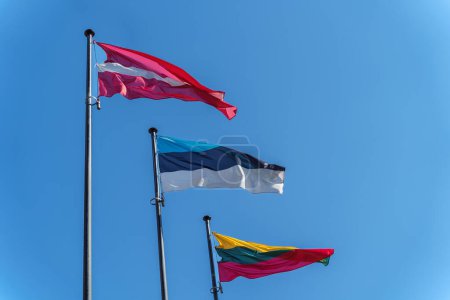 Lettische, estnische und litauische Flaggen an Fahnenmasten vor blauem Himmel.