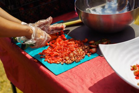 Hände eines Menschen in Einmalhandschuhen schneiden reife Erdbeeren auf einem Tisch im Garten, um Marmelade, sommerliche Desserts oder ein Getränk zuzubereiten. Der Prozess der Herstellung von hausgemachten Konfitüren, Marmelade, Konserven.