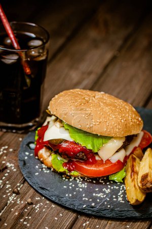 Photo for Closeup homemade beef burgers with a glass of soda, baked potato, tomatoes, cheese, sauce on wooden table. Selective focus. Delicious food. - Royalty Free Image