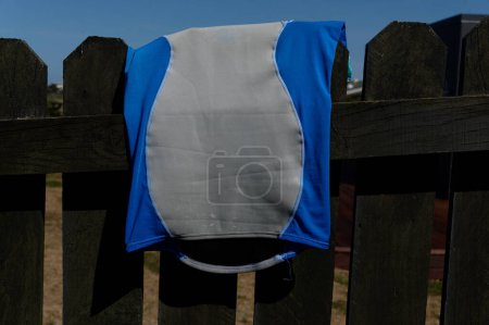 Photo for A blue and grey rash shirt has been flung over a fence to dry. - Royalty Free Image