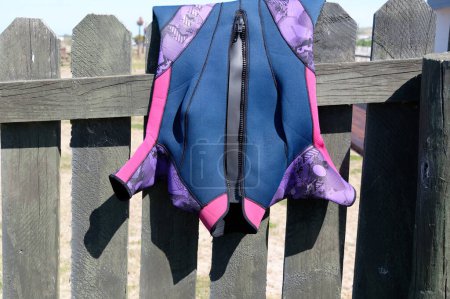 Photo for A wetsuite has been thrown over a fence to dry out. It is a shorty, short arms and legs. Its zip is undone to help the drying process. - Royalty Free Image