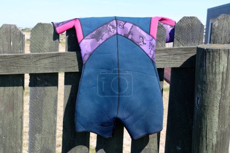Photo for A blue, purple and pink shorty wetsuit has been hung over a fence to day after being used. - Royalty Free Image