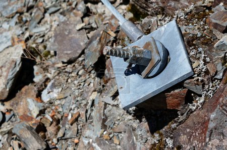 A large bolt and square plate has been driven into the ground to hold a cable.