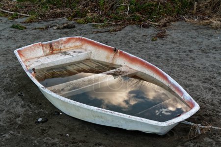 A neglected little dingy sits on the sand waiting to be bailed out.