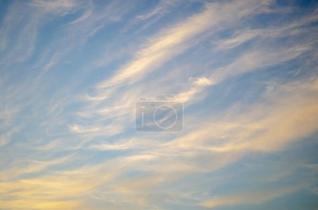 Téléchargez les photos : Une photo envoûtante capturant le ciel bleu serein orné de beaux nuages de cirrus blancs et jaunes lors d'un coucher de soleil captivant. - en image libre de droit