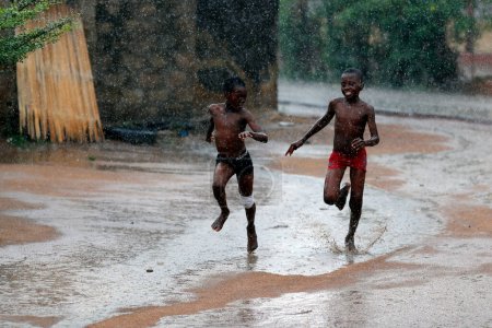 Téléchargez les photos : Rainy season in an african village. Boys running under the rain Togo. - en image libre de droit