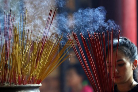 Ong Bon Pagoda, Taoist Temple.  Woman praying with burning incense sticks. Ho Chi Minh City. Vietnam.