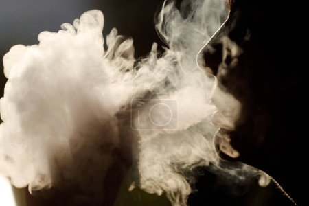 Téléchargez les photos : Profil silhouette d'une femme qui fume. Fumée blanche intense. Une cigarette électronique. France. - en image libre de droit