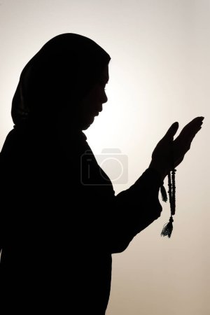 Téléchargez les photos : Silhouette de femme musulmane tenant des perles de prière dans ses mains et priant contre le ciel. Religion concept de prière - en image libre de droit