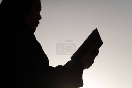 Téléchargez les photos : Silhouette de femme musulmane lisant le noble Coran contre le ciel. Religion concept de prière - en image libre de droit