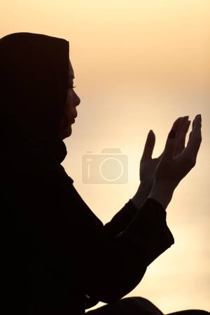 Téléchargez les photos : Silhouette de femme musulmane en abaya priant les mains en l'air au coucher du soleil. Religion concept de prière. - en image libre de droit