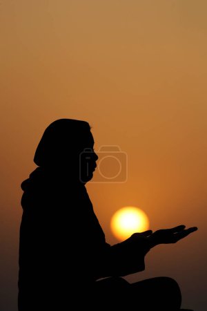 Téléchargez les photos : Silhouette de femme musulmane en abaya priant avec ses mains au coucher du soleil. Religion concept de prière. - en image libre de droit