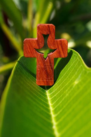 Photo for Close-up shot of a christian cross with holy spirit on a fresh green magnolia leave. Faith and spirituality. - Royalty Free Image