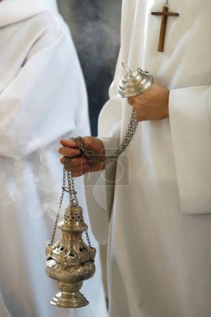 Catholic church.  Altar boy shaking a censer to produce smoke and fragrance of incense.  France.