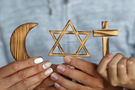 Photo for Religious symbols in three hands. Jewish Star of David, Muslim star and Crescent, Christian Cross. Religion, interreligious  and interfaith dialogue concept. - Royalty Free Image