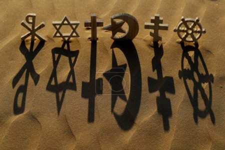 Religious symbols on sand at sunset :  Catholic, Islam, Judaism, Orthodoxy, Protestant, Buddhism and Hinduism. Interreligious, interfaith and spirituality concept.