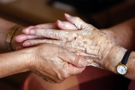 Altenheim. Pflegehelferinnen reichen beruhigende Seniorin die Hand.