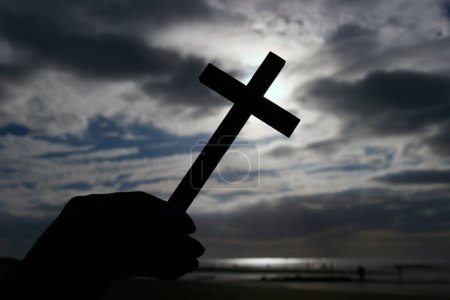 Foto de Hombre sosteniendo una cruz cristiana contra el cielo nublado de Darrk. Símbolo religioso del cristianismo - Imagen libre de derechos
