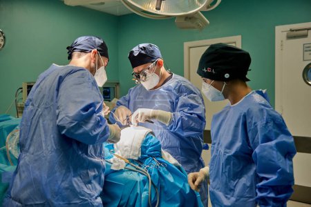 Téléchargez les photos : Diverse men and women in disposable uniform doing surgery on patient in sterile operating room during work in modern hospital - en image libre de droit