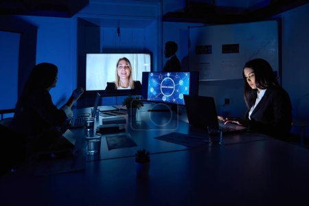 Téléchargez les photos : Travailleuses attentives méconnaissables avec netbooks à table pendant l'appel vidéo sur moniteur dans l'espace de travail - en image libre de droit