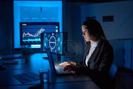 Photo for Side view of attentive female analyst working on netbook at desk with diagram and blockchain technology illustration on monitors - Royalty Free Image